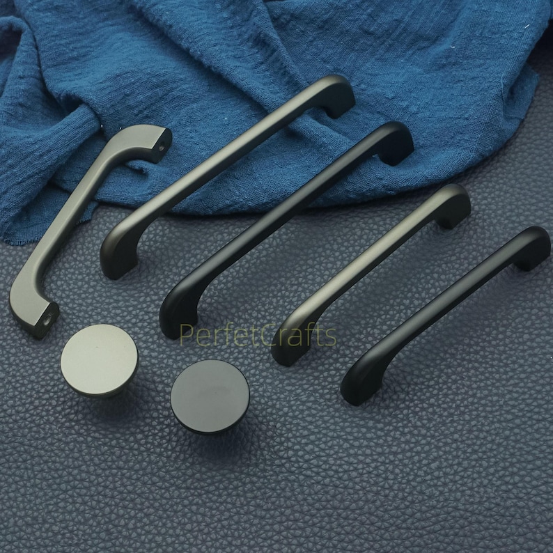 Op de afbeelding: Een selectie van kastbeslag, waaronder handgrepen en ronde knoppen, in verschillende maten en afwerkingen. Het beslag is in grijstinten en zwart, met een matte afwerking. De tekst "Perfectcrafts" is zichtbaar.