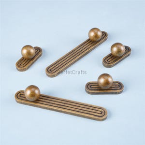 Könnte beinhalten: Eine Sammlung von Möbelgriffen und -knöpfen in Bronzetönen. Die Griffe haben eine rechteckige Basis mit drei parallelen Rillen und einen kugelförmigen Knopf. Die Knöpfe haben eine ovale Basis mit einer einzelnen Rille und einem kugelförmigen Knopf.