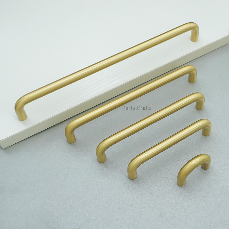 May include: A selection of gold-toned cabinet handles in different lengths. The handles are straight with rounded ends, displayed on a white surface. The text "PerfetcCrafts" is visible on the image.