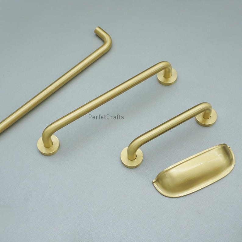 May include: A selection of brass-toned cabinet handles and a cup pull. The image shows various sizes of bar pulls with curved ends and a smooth finish. The hardware is presented on a neutral grey backdrop.