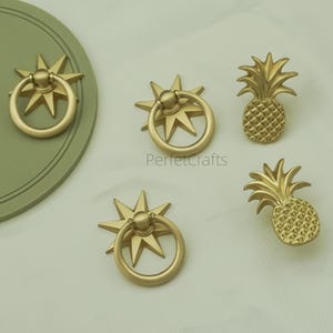 May include: Gold-coloured cabinet hardware featuring starburst ring pulls and pineapple-shaped knobs. The hardware is displayed on a light background. The text "PerfetcCrafts" is visible on the image.