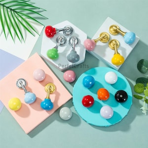 May include: A collection of colorful cabinet knobs and pulls in various colors, including red, green, gray, pink, yellow, blue, orange, white, and black. Some knobs have silver or gold hardware. The text "PerfecCrafts" is visible.