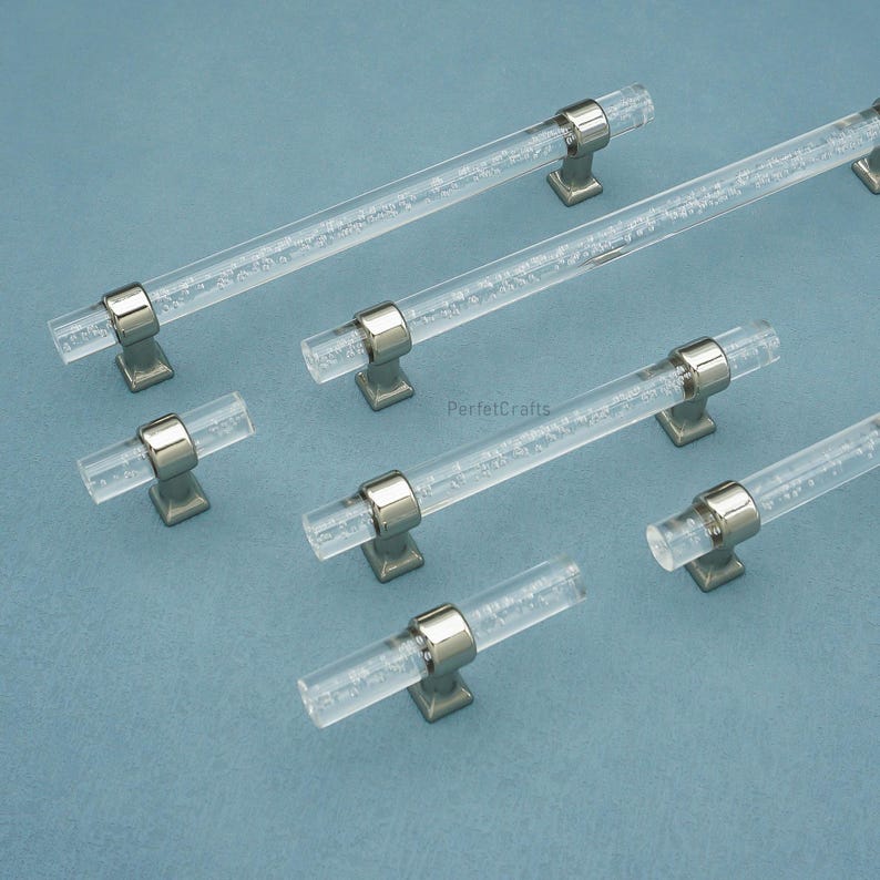 Peut inclure: Poign&eacute;es de meubles en acrylique transparent avec des accents m&eacute;talliques argent&eacute;s. Les poign&eacute;es cylindriques pr&eacute;sentent un design int&eacute;rieur &agrave; bulles. Les poign&eacute;es sont mont&eacute;es sur des bases carr&eacute;es. L'image est sur un fond bleu clair.