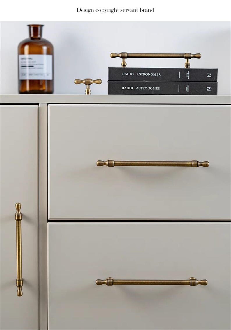 May include: A selection of antique brass cabinet handles and knobs, shown on a light grey cabinet. The hardware has a vintage appearance with a warm, aged finish. The image also includes a brown glass bottle and two black books. The text "RADIO ASTRONOMER" is visible.