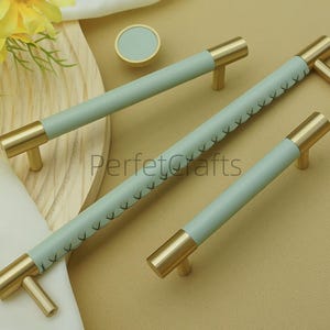 Puede incluir: Un juego de herrajes para gabinetes con tiradores de lat&oacute;n y empu&ntilde;aduras de cuero azul claro. Los tiradores m&aacute;s largos tienen costuras decorativas. Tambi&eacute;n se incluye un pomo redondo a juego.