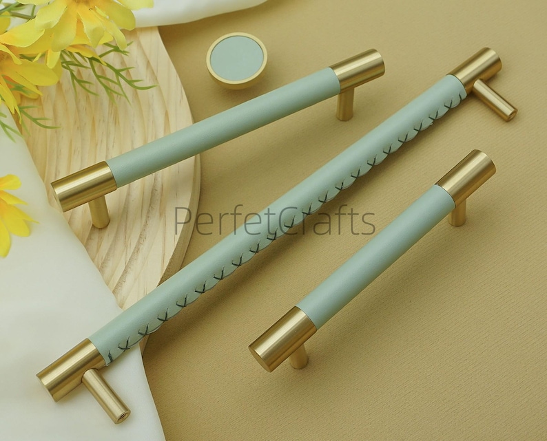 Puede incluir: Un juego de herrajes para gabinetes con tiradores de lat&oacute;n y empu&ntilde;aduras de cuero azul claro. Los tiradores m&aacute;s largos tienen costuras decorativas. Tambi&eacute;n se incluye un pomo redondo a juego.