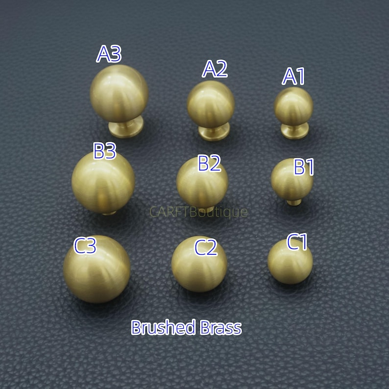 Puede incluir: Nueve pomos de armario de lat&oacute;n cepillado de varios tama&ntilde;os est&aacute;n dispuestos sobre una superficie oscura. Los pomos est&aacute;n etiquetados A1, A2, A3, B1, B2, B3, C1, C2 y C3. El texto "Brushed Brass" est&aacute; debajo.