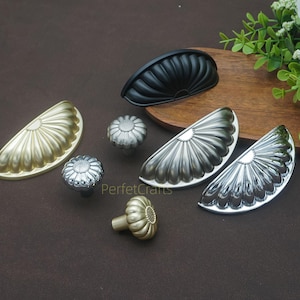 May include: A selection of decorative cabinet hardware, including drawer pulls and knobs. The hardware features gold, silver, and black finishes. Designs include half-moon pulls and flower-shaped knobs. Ideal for kitchen or furniture upgrades.