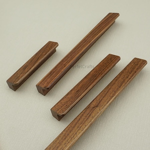 May include: A collection of wooden cabinet pulls in various sizes. The pulls are a rich brown color with a rectangular shape and a beveled edge. The wood grain is visible, adding texture to the design. These pulls are suitable for drawers and cabinets.