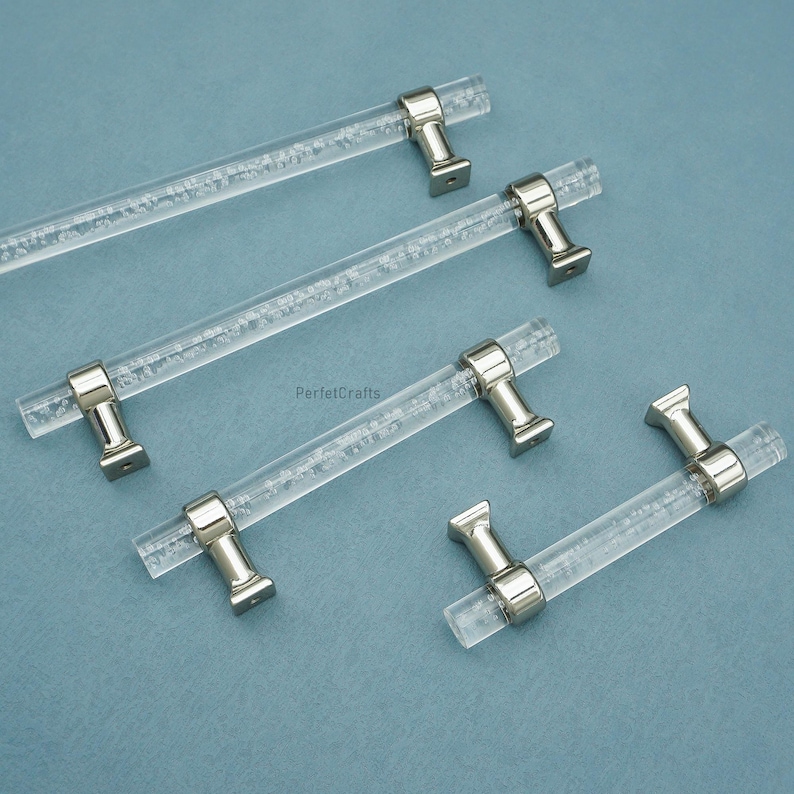 Peut inclure: Poign&eacute;es de meubles en acrylique transparent avec des fixations en m&eacute;tal argent&eacute;. Les poign&eacute;es sont dispos&eacute;es sur une surface bleu clair. Les tiges en acrylique ont un aspect textur&eacute;, semblable &agrave; des bulles. Les fixations sont rectangulaires avec un dessus arrondi.