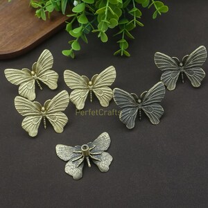 May include: A collection of decorative butterfly-shaped hardware in various metallic finishes. The butterflies are detailed with textured wings and are likely used as drawer pulls or cabinet knobs. The image includes the text "PerfetcCrafts".