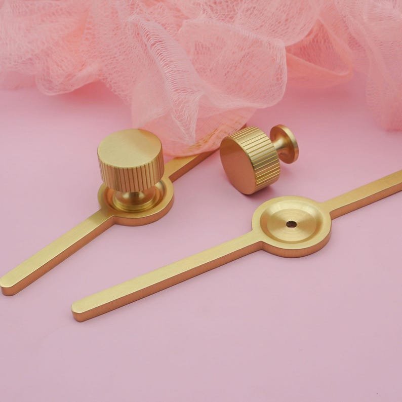 Puede incluir: Juego de herrajes dorados para armarios. El juego incluye dos pomos y dos tiradores. Los pomos tienen forma cil&iacute;ndrica con ranuras verticales. Los tiradores tienen un dise&ntilde;o lineal con un detalle circular en el centro.