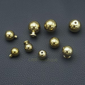 Puede incluir: Una colecci&oacute;n de tiradores y pomos dorados y brillantes de varios tama&ntilde;os. Los herrajes tienen un acabado pulido y reflectante, algunos con forma de bola y otros con un v&aacute;stago para la fijaci&oacute;n. Los art&iacute;culos est&aacute;n dispuestos sobre una superficie gris oscuro.