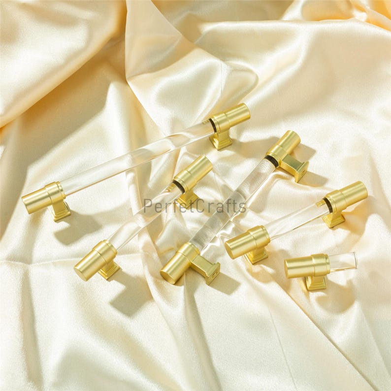May include: Several cabinet pulls with clear acrylic rods and gold-colored metal hardware. The pulls are arranged on a cream-colored satin fabric. The text "PerfectCrafts" is visible on the fabric.