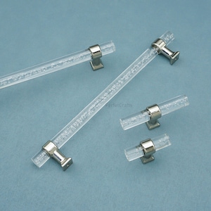 Peut inclure: Poign&eacute;es de meubles en acrylique transparent avec des bases en m&eacute;tal argent&eacute;. Les poign&eacute;es ont une forme cylindrique avec une texture &agrave; bulles &agrave; l'int&eacute;rieur. L'image montre quatre poign&eacute;es et deux tirettes sur fond bleu clair. Le texte "PerfectCrafts" est visible.
