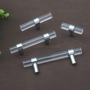 May include: A white ceramic mug with a black handle and the text "But First, Coffee" in a bold, black font. The mug is set against a blurred background, suggesting a cosy setting.