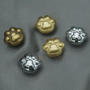 May include: Five paw-shaped cabinet knobs in gold and silver finishes. The knobs are arranged on a grey surface. The text "PerfetcCrafts" is visible on the image.