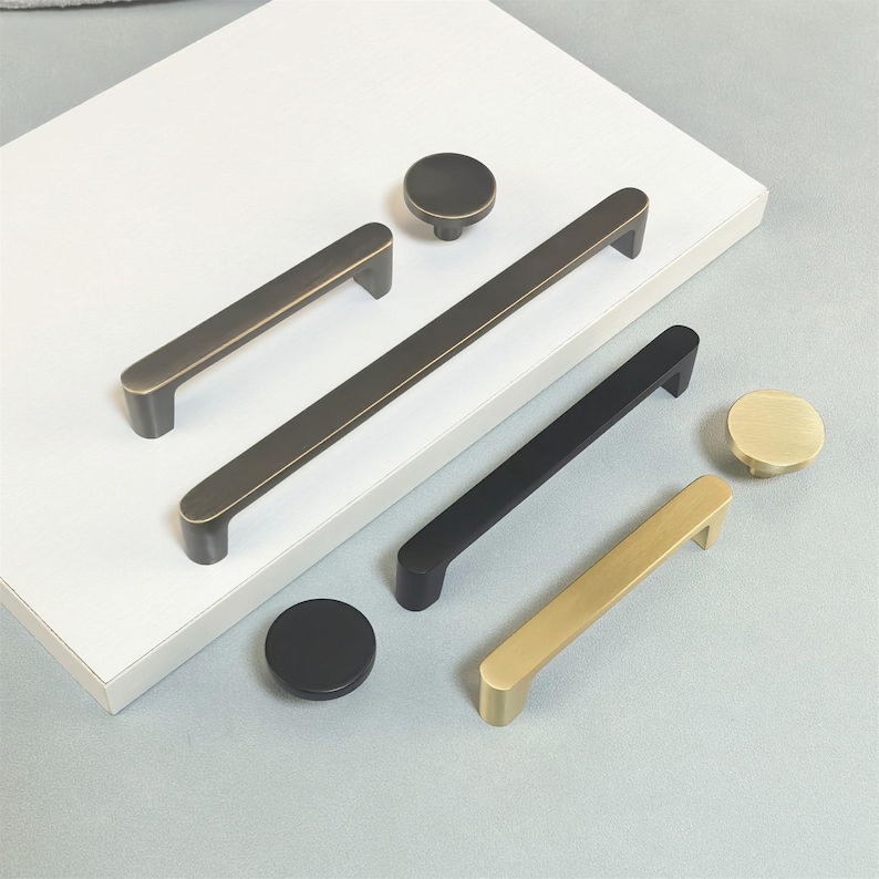 May include: A collection of cabinet hardware, including handles and knobs, in various finishes. The selection includes dark bronze, matte black, and brushed gold options. The handles vary in length, with the longest being approximately 12 inches.