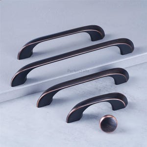 May include: A set of bronze-colored cabinet hardware, including four handles and one knob. The handles have a curved design with a dark finish and copper-colored accents. The knob is round with a matching finish. The brand name "PerfetcCrafts" is visible.