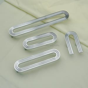 May include: A selection of silver cabinet pulls in different sizes. The pulls feature a grooved, oval design with a curved handle. The image includes the text "PerfetcCrafts".