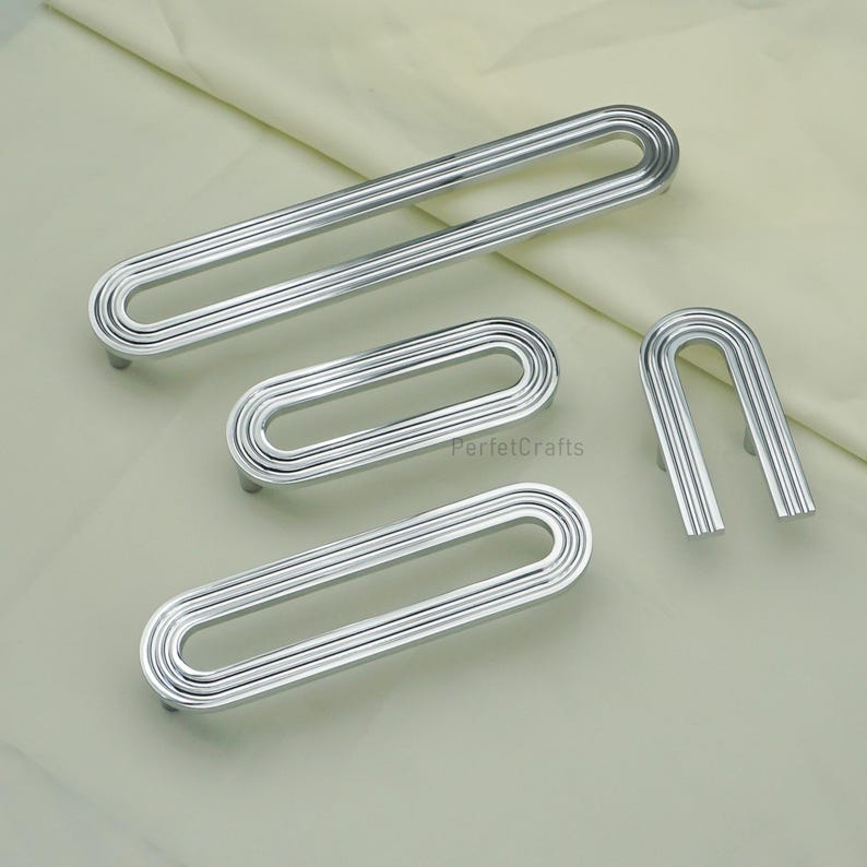 May include: A selection of silver cabinet pulls in different sizes. The pulls feature a grooved, oval design with a curved handle. The image includes the text "PerfetcCrafts".