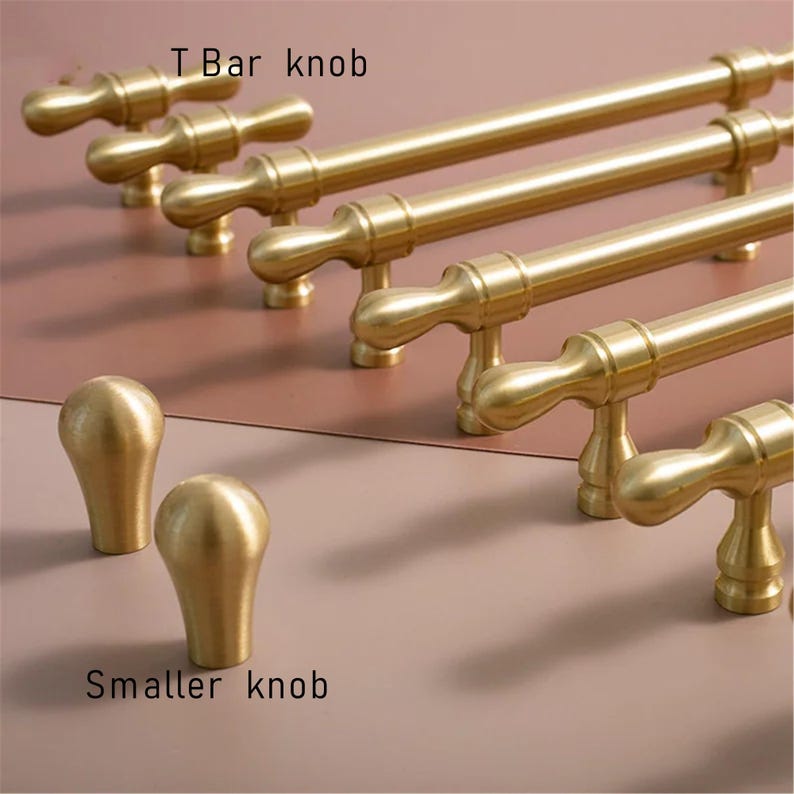 May include: A selection of gold-coloured cabinet hardware is shown, including T-bar knobs and smaller knobs. The T-bar knobs are long and cylindrical with a rounded handle. The smaller knobs have a rounded, teardrop shape. The text "T Bar knob" and "Smaller knob" are visible.