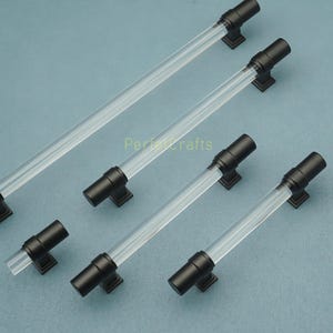 May include: A collection of cabinet pulls with clear acrylic rods and matte black hardware. The pulls have a modern design and are arranged on a light blue surface. The text "Perfect Crafts" is visible.