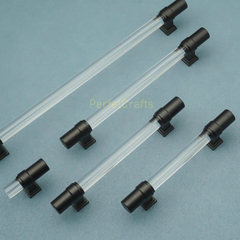 May include: A collection of cabinet pulls with clear acrylic rods and matte black hardware. The pulls have a modern design and are arranged on a light blue surface. The text "Perfect Crafts" is visible.