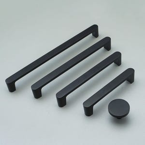 May include: A set of matte black cabinet handles and a knob. The set includes four rectangular bar pulls of different lengths and a circular knob. The hardware is displayed on a light grey surface, showcasing a modern design.