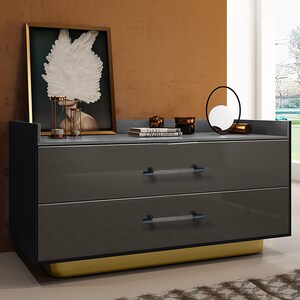 May include: A modern gray dresser with two drawers and crystal-like handles. The dresser has a yellow base and a dark gray top. A framed artwork and decorative items sit on top of the dresser.