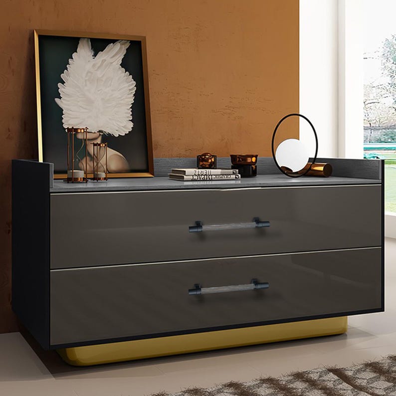 May include: A modern gray dresser with two drawers and crystal-like handles. The dresser has a yellow base and a dark gray top. A framed artwork and decorative items sit on top of the dresser.