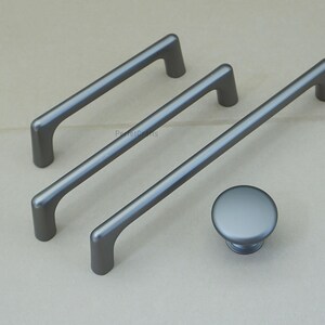 May include: A set of three gray cabinet pulls and a matching knob. The pulls are bar-shaped with rounded ends, and the knob is a simple, circular design. All hardware has a matte finish.