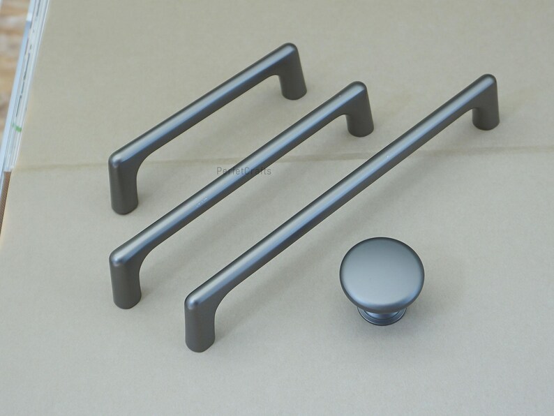 May include: A set of three gray cabinet pulls and a matching knob. The pulls are bar-shaped with rounded ends, and the knob is a simple, circular design. All hardware has a matte finish.