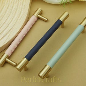 Puede incluir: Tres tiradores de armario con herrajes de lat&oacute;n y secciones centrales de colores. Los tiradores tienen un centro rosa, azul marino y azul claro. El texto "PerfetcCrafts" es visible en la esquina inferior derecha.