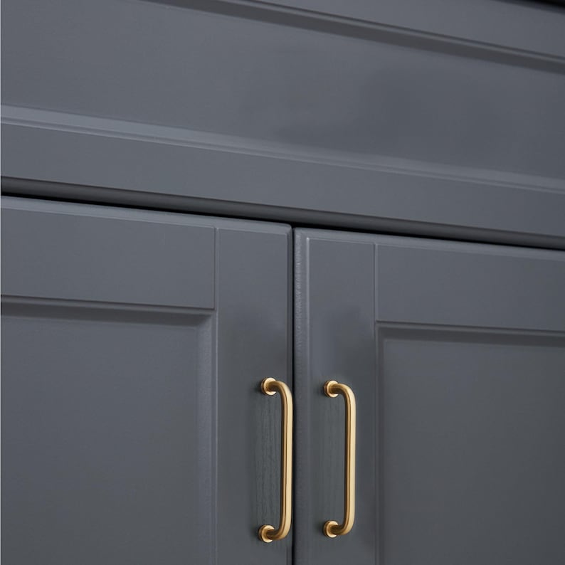 May include: Close-up of a section of a grey cabinet with two gold-coloured, curved bar handles. The cabinet doors are painted a solid grey colour. The handles are mounted vertically on the cabinet doors.
