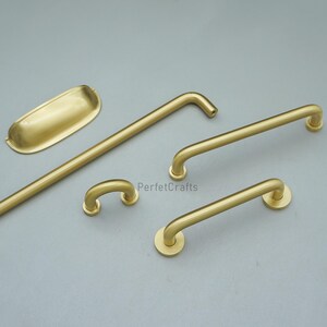 May include: A selection of brass-coloured cabinet hardware, including handles and a pull. The hardware has a matte finish and various shapes, including curved and straight designs. The text "PerfetcCrafts" is visible.