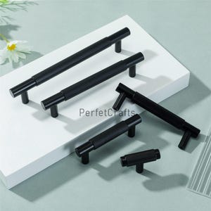 May include: A collection of black cabinet pulls with a textured, diamond-patterned grip. The pulls are in various sizes and have a T-bar design. The image includes the text "PerfektCrafts".