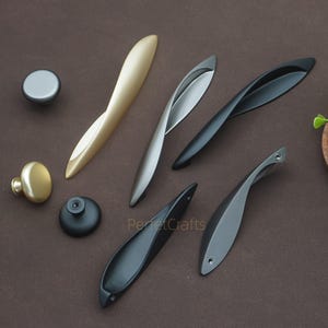 以下が含まれることがあります： さまざまな金属仕上げのキャビネットハードウェアのコレクション。 金、銀、黒のオプションがあり、さまざまな形状とデザインがあります。 画像には「PerfectCrafts」というテキストが含まれています。