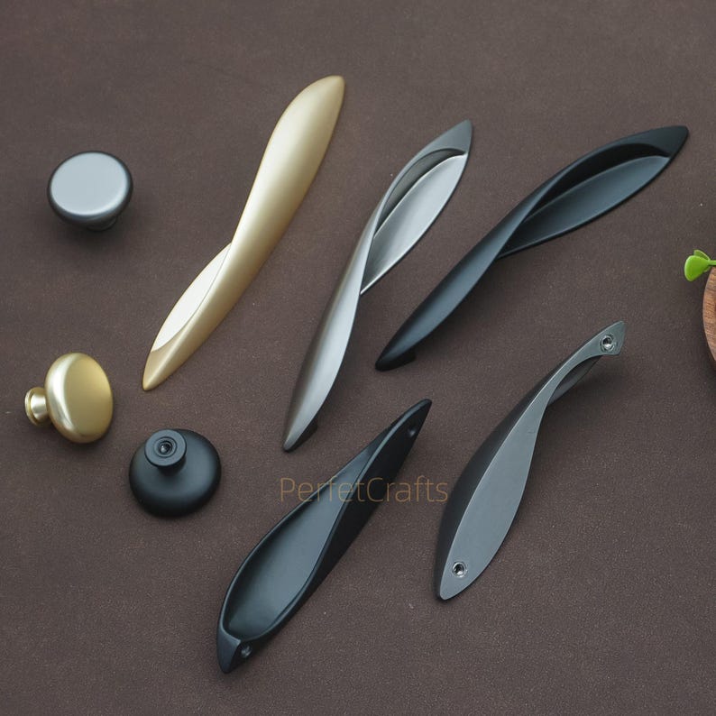 以下が含まれることがあります： さまざまな金属仕上げのキャビネットハードウェアのコレクション。 金、銀、黒のオプションがあり、さまざまな形状とデザインがあります。 画像には「PerfectCrafts」というテキストが含まれています。