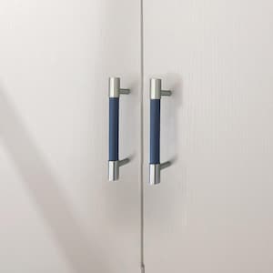 Puede incluir: Dos tiradores de armario con un dise&ntilde;o moderno. Cada tirador presenta un agarre cil&iacute;ndrico azul marino, flanqueado por extremos y postes de montaje de metal plateado cepillado. Montados en una puerta de armario blanca.