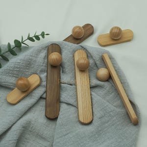 May include: A selection of wooden cabinet knobs and pulls in different shapes and shades. The knobs are spherical, and the pulls are rectangular. Some are light-coloured, while others are a darker brown. They are arranged on a grey fabric.