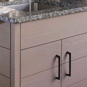 May include: Close-up of a light-colored wooden cabinet with black handles. The cabinet has a granite countertop and a stainless steel sink. The cabinet doors have a horizontal plank design.