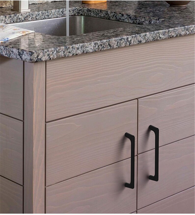 May include: Close-up of a light-colored wooden cabinet with black handles. The cabinet has a granite countertop and a stainless steel sink. The cabinet doors have a horizontal plank design.