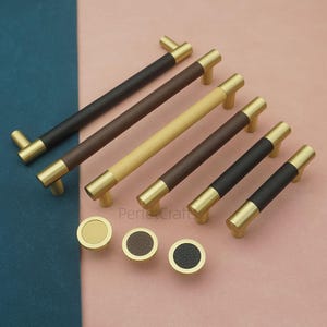 Pode incluir: Uma coleção de ferragens para armários, incluindo várias puxadores longos e puxadores redondos. Os puxadores apresentam extremidades de cor latão e centros revestidos em couro em várias cores, incluindo preto, castanho e bege. Os puxadores têm um acabamento em latão a condizer.