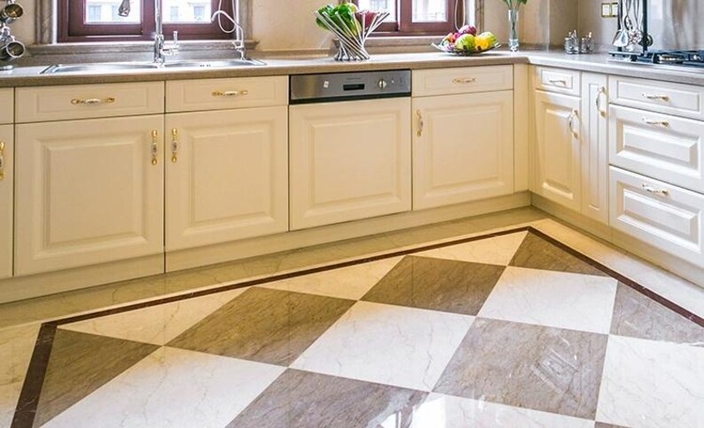 Pu&ograve; includere: Cucina luminosa con mobili color crema e lavastoviglie in acciaio inossidabile. Il pavimento presenta un motivo a scacchi nei toni del grigio e del bianco, incorniciato da un bordo scuro. La cucina ha un lavandino e una finestra.