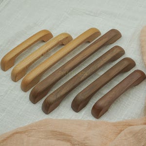 May include: A collection of wooden cabinet pulls in varying shades of brown. The pulls are arranged in a row, showcasing the natural wood grain and smooth finish. The pulls are approximately 5 to 7 inches in length.