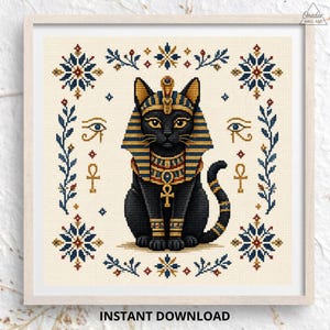 May include: A cross-stitch pattern featuring a black cat adorned with an Egyptian-style headdress and collar, centered among symbols including the Eye of Horus, ankhs, and floral motifs, all set against a cream-colored grid background.