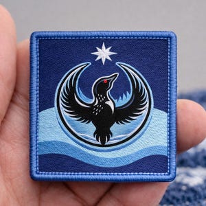 May include: Square patch with a blue background and a detailed design. The patch features a black bird with outstretched wings, a red eye, and a white star. Below the bird are blue wavy lines. The patch is bordered with blue stitching.