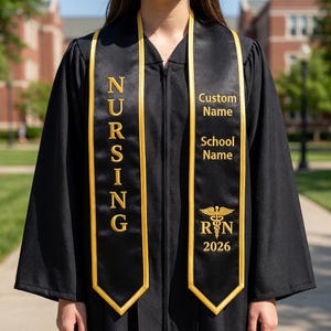 May include: Black graduation gown with gold trim and a gold "NURSING" sash. The sash has a gold border and includes the text "Custom Name", "School Name", the RN symbol, and the year 2026.