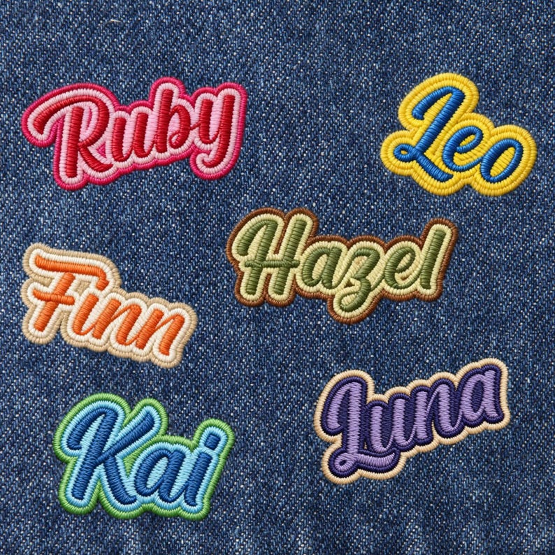 May include: Embroidered name patches in various colors, including Ruby, Leo, Finn, Hazel, Kai, and Luna. Each patch features a unique color scheme and a cursive font, perfect for personalizing clothing or accessories. The patches are set against a denim background.